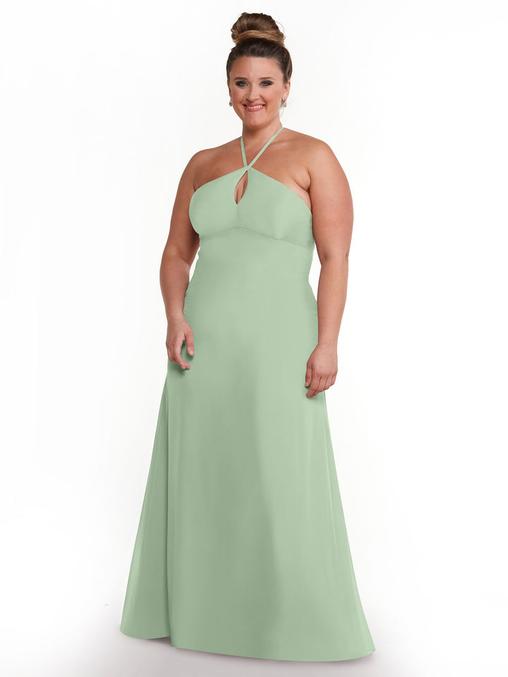 A woman stands smiling against a white background, modeling the Avery Austin TH-80137 dress in Dusty Sage—a minimalistic, floor-length halter gown with a keyhole neckline and subtle keyhole back.