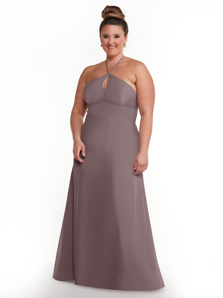A woman smiles against a white background wearing Avery Austin’s 80137—a mauve, floor-length halter dress with a keyhole back. Her hair is in a high bun and she accessorizes with earrings.