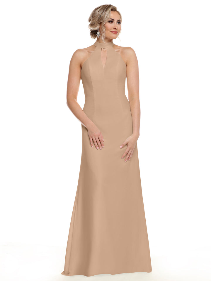 A woman with blonde hair in an updo models Avery Austin’s 80138, a sleeveless, floor-length beige gown with a halter neckline and keyhole detail, standing against a plain white background.