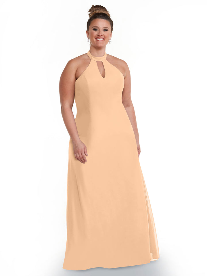 A woman with brown hair in a bun wears Avery Austin’s 80138, a peach sleeveless floor-length gown with a halter neckline and open back, standing and smiling against a plain white background.