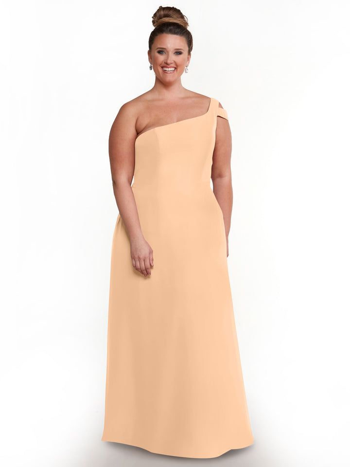 A woman smiles in the Avery Austin 80139 dress, a sleeveless, blush one-shoulder gown with a side slit. Her hair is in a neat bun, she wears dangling earrings, and the background is plain white.