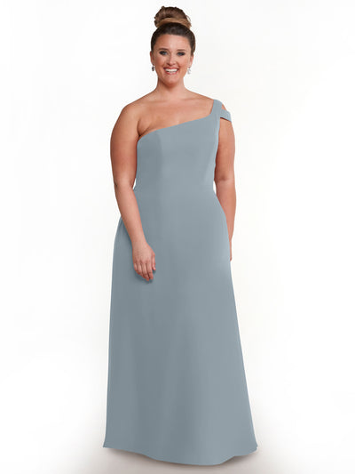 A woman wearing Avery Austin’s 80139, a light blue floor-length one shoulder dress, stands smiling against a white background with her hair in a bun and earrings.