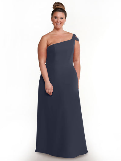 A woman smiles against a white background, wearing Avery Austin’s sophisticated dark blue one shoulder dress (style 80139), her hair in a neat bun and accessorized with elegant drop earrings.