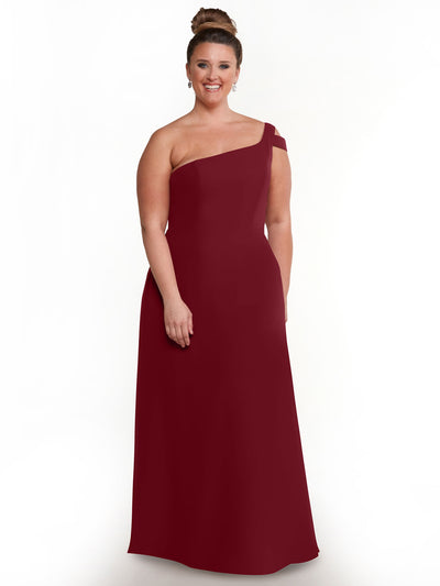 A woman stands smiling in Avery Austin style 80139—a sleeveless, floor-length burgundy one-shoulder dress with an asymmetrical neckline and side slit—posed against a plain white background.