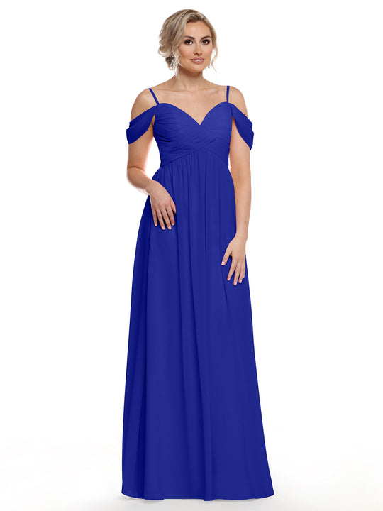 A woman in the Avery Austin 80142, a cobalt floor-length cold shoulder dress with thin straps and off-the-shoulder sleeves, stands against a white background. Her blonde hair is styled up as she gazes slightly to the side.