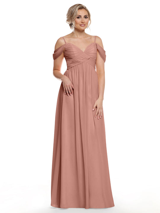 A woman stands against a white background wearing Avery Austin’s TH-80142—a long, dusty rose chiffon dress with an off-the-shoulder sweetheart neckline and pleated bodice. She has styled blonde hair and statement earrings.