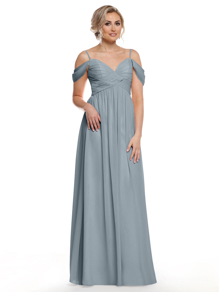 A woman with blonde hair styled up wears Avery Austin’s 80142, a dusty blue floor-length cold shoulder dress with spaghetti straps, posing against a white background in effortless boho chic style.