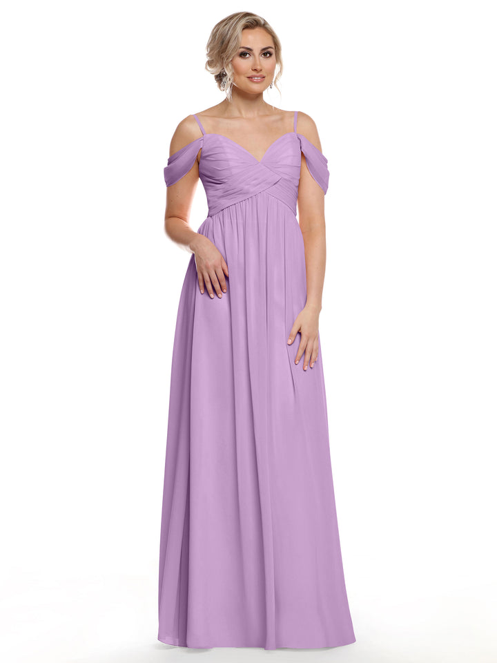 A woman wearing Avery Austin’s floor-length lilac chiffon dress, style 80142 with spaghetti straps, stands against a white background, gazing ahead with one hand resting lightly at her side.
