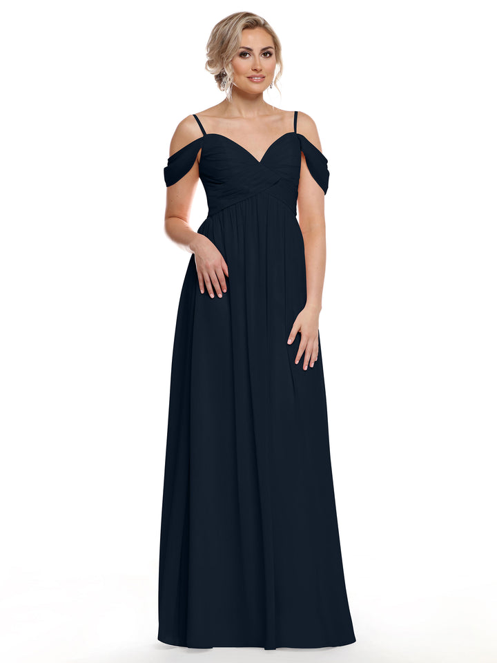 A woman stands against a plain white background wearing Avery Austin 80142, a floor-length midnight chiffon cold shoulder dress with spaghetti straps. Her blonde hair is styled up, and she looks forward with one hand by her side.