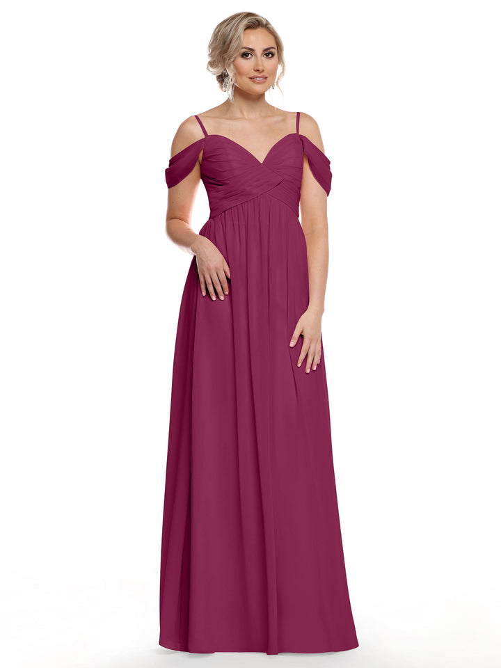 A woman wearing Avery Austin’s floor-length, plum chiffon cold shoulder dress (style 80142) with thin straps and a sweetheart neckline stands against a plain white background.