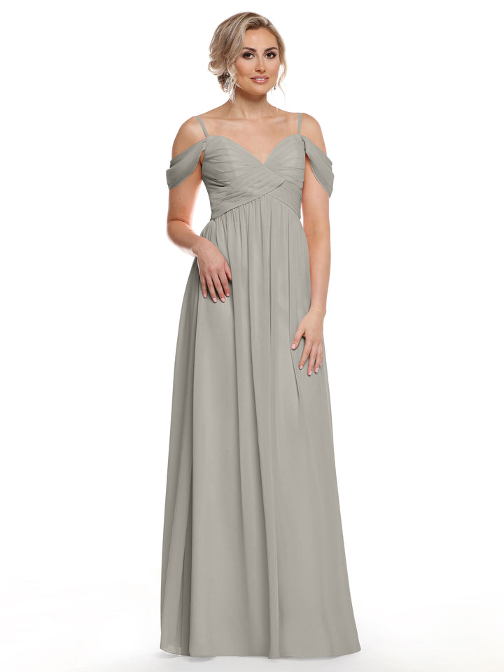 A woman stands against a white background in the Avery Austin 80142—an elegant silver, floor-length chiffon dress with spaghetti straps and a ruched bodice, perfectly capturing effortless boho chic style.