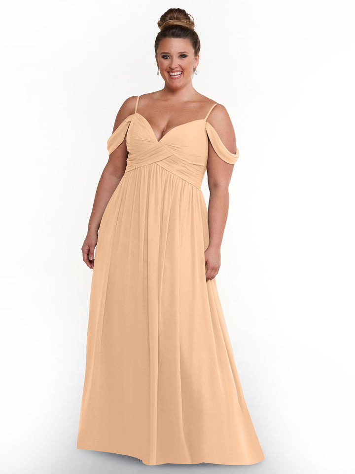 A smiling woman wears the Avery Austin 80142, a floor-length blush chiffon dress with spaghetti straps and off-the-shoulder sleeves, standing against a plain white background.