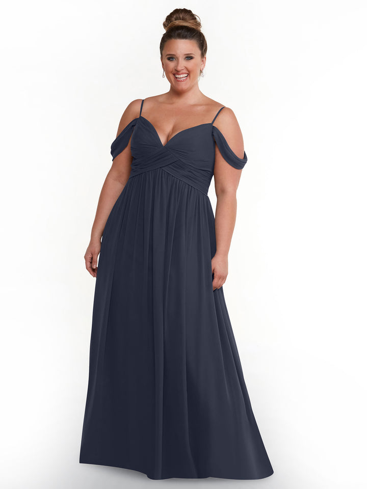 A woman smiles against a plain white background wearing Avery Austin’s 80142, a navy blue, floor-length boho chic off-the-shoulder gown with spaghetti straps.