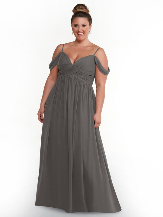 A smiling woman with her hair in a bun models the Avery Austin TH-80142, a floor-length cold shoulder dress in slate gray with spaghetti straps and a ruched bodice, standing against a plain white background.