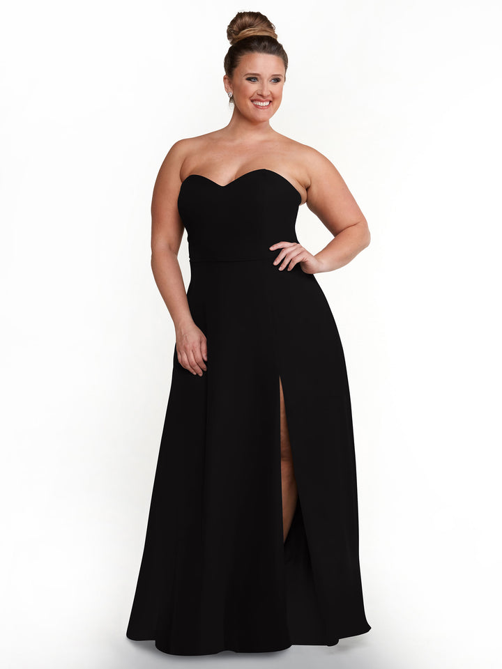 A woman in the Avery Austin 80143 strapless sweetheart dress with sash back and thigh-high side slit stands against a white background, smiling with her hair in a neat bun.