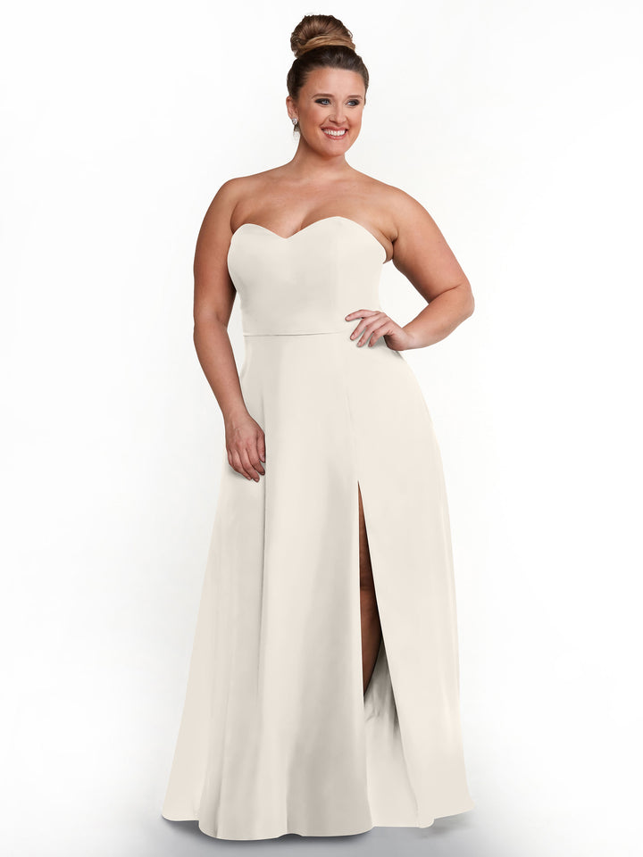 A woman models the Avery Austin 80143 strapless sweetheart dress with a sash back and high side slit, posing with one hand on her hip against a plain white background.