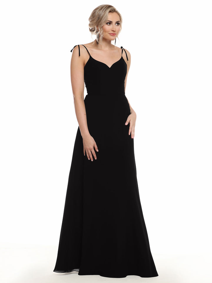 A woman with blonde loose curls wears the Avery Austin 80144—a long, black chiffon dress with thin shoulder straps and a fitted bodice. She stands against a plain white background, gazing slightly to the side.