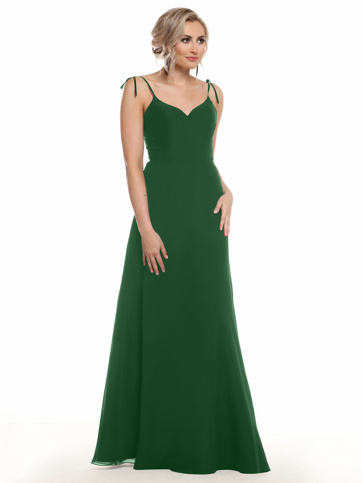 A woman wears Avery Austin’s 80144: a sleeveless, floor-length dark green chiffon dress with a V-neck and thin shoulder straps tied in bows, standing against a white background.