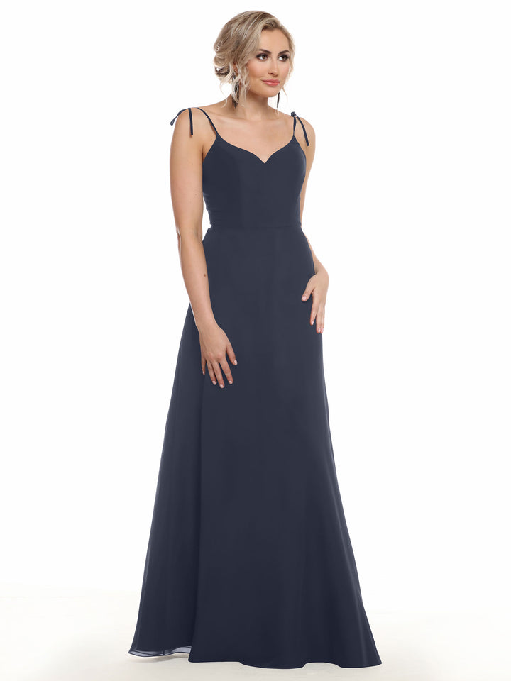 Model wears Avery Austin 80144, a navy sleeveless chiffon dress with thin straps and V-neck. She stands against a white background, her short wavy blonde hair styled up, gazing slightly to the side.
