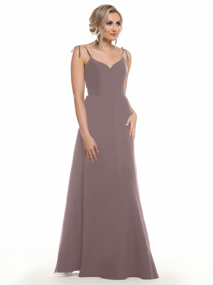 A woman with light wavy hair wears Avery Austin’s 80144: a sleeveless, mauve V-neck chiffon dress with thin straps, standing against a plain white background and looking slightly to the side.