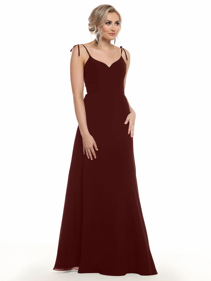 A woman in the Avery Austin TH-80144, a floor-length burgundy chiffon dress with thin straps and a subtle V-neck, stands against a white background. She has light hair in loose waves and a neutral expression.