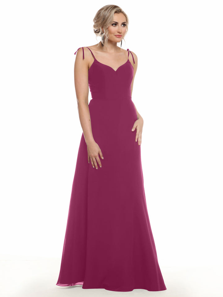 A woman wears the Avery Austin 80144, a sleeveless magenta chiffon gown with thin straps and a V-neck, standing against a white background. She has short wavy blonde hair styled up and keeps one hand by her side with a neutral expression.