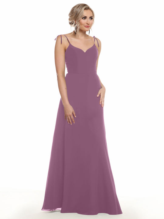A woman with blonde hair in an updo wears the Avery Austin 80144, a floor-length mauve chiffon dress with thin straps, fitted bodice, and subtle V-neck. She stands against a plain white background, looking slightly to the side.