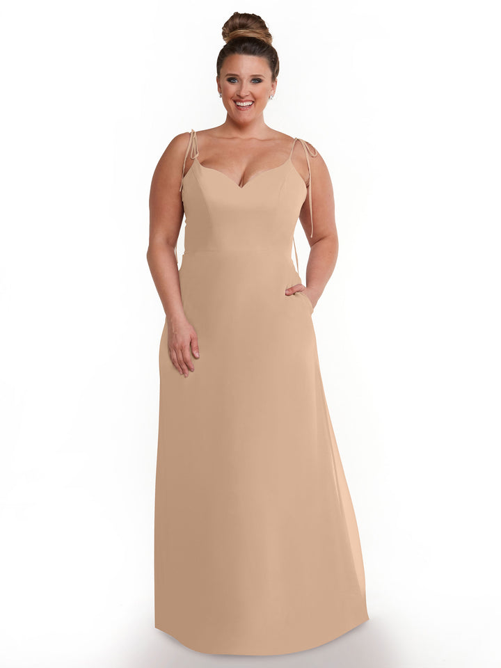 A woman with hair in a high bun models Avery Austin style 80144, a sleeveless, floor-length chiffon dress with thin straps and a V-neckline, posing against a plain white background.