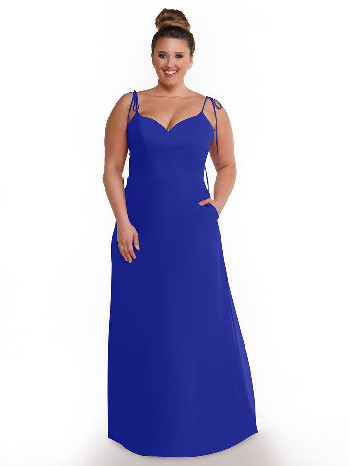 A woman with brown hair in a bun smiles while wearing Avery Austin’s 80144 royal blue chiffon dress, featuring thin straps and a sweetheart neckline, as she stands against a plain white background.