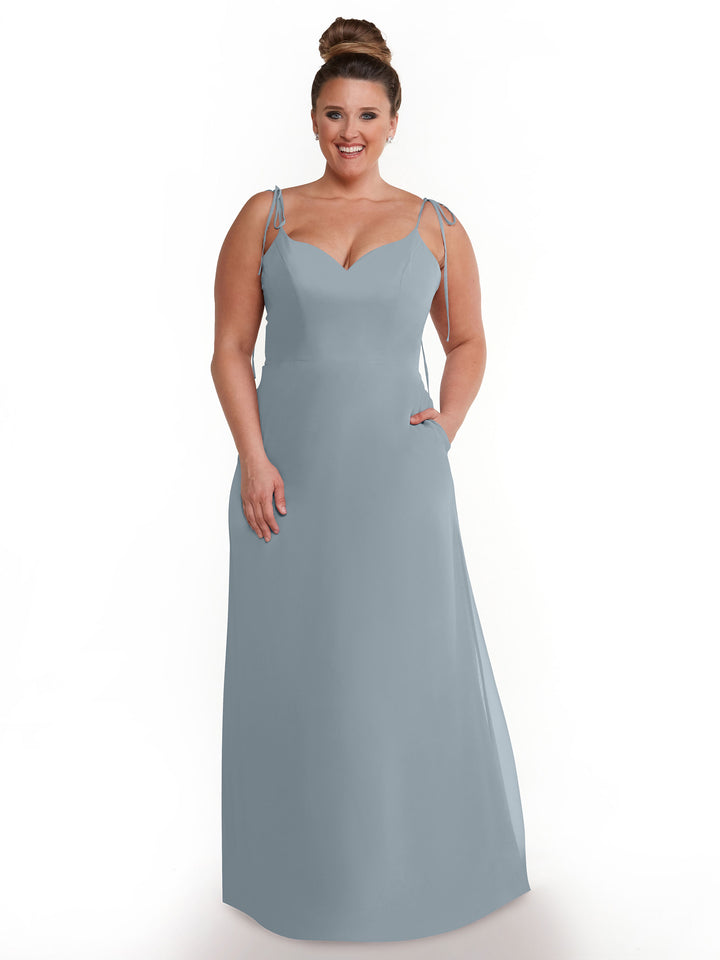 A woman with brown hair in a high bun models the Avery Austin 80144—a long light blue chiffon dress with thin straps and a sweetheart neckline—standing against a plain white background.