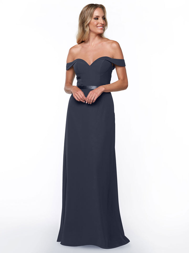 A woman in the Avery Austin 80145, a floor-length off-the-shoulder bridesmaid dress with a sweetheart neckline, stands against a white background, smiling gently with her hands clasped in front of her.