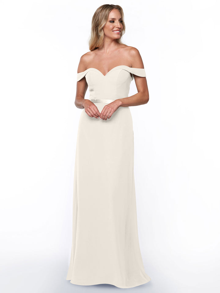 A woman stands smiling with hands clasped, wearing the Avery Austin 80145 long, off-the-shoulder bridesmaid dress in ivory against a plain white background.