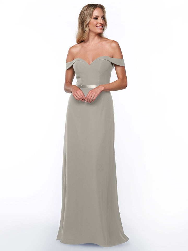 A woman models Avery Austin’s 80145, a light gray off-the-shoulder bridesmaid dress with a sweetheart neckline and fitted bodice. The floor-length chiffon gown flatters her figure as she smiles, wavy blonde hair loose against a white background.