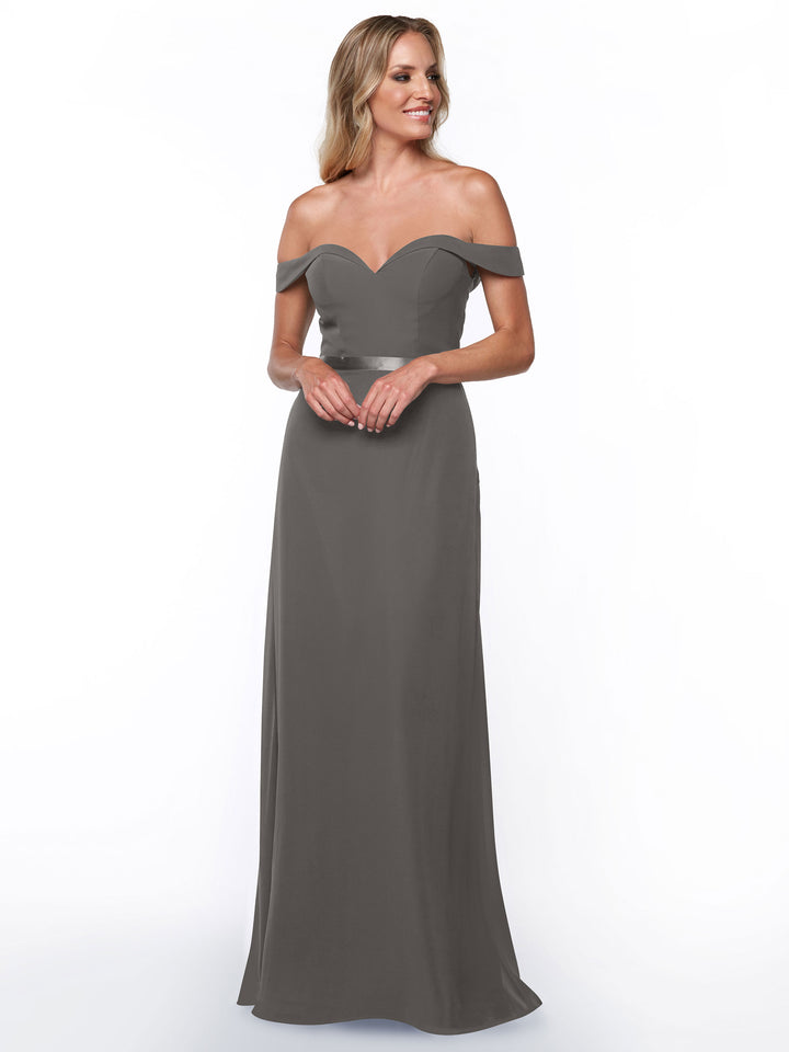 A woman stands and smiles against a plain white background, wearing the Avery Austin 80145: a floor-length, off-the-shoulder bridesmaid dress with a fitted bodice and short sleeves.