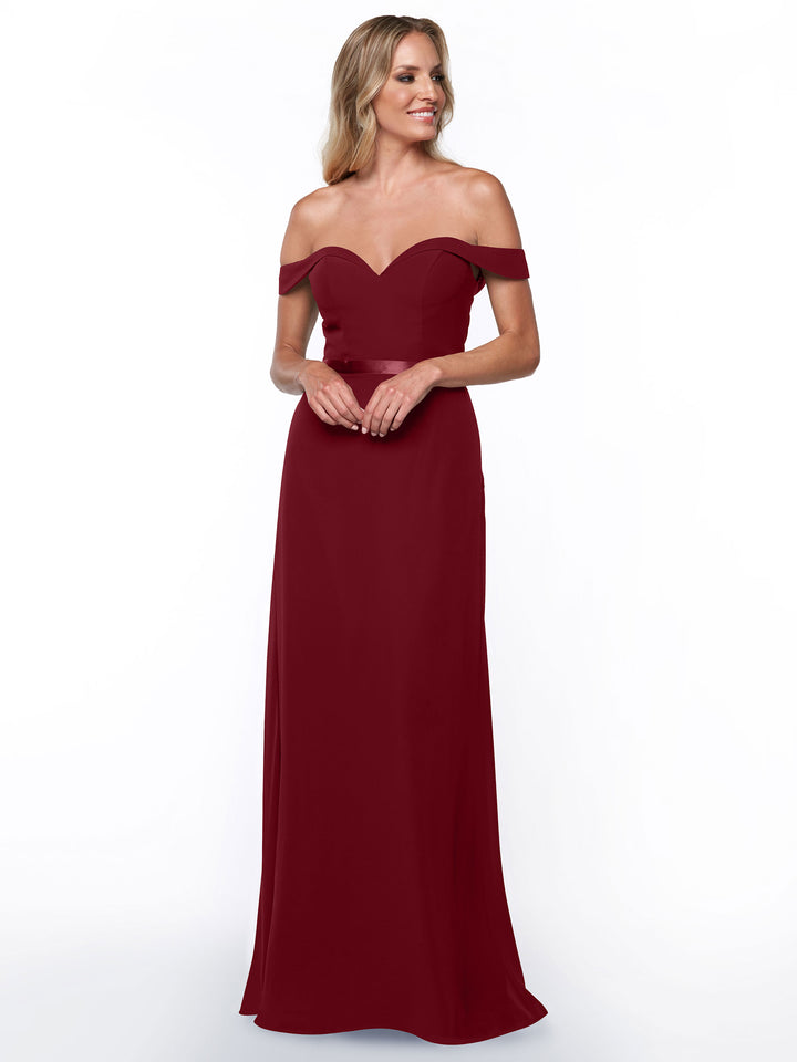 A woman smiles with hands clasped in front, modeling the Avery Austin TH-80145 off-the-shoulder bridesmaid dress in wine, floor-length style, against a plain white background.