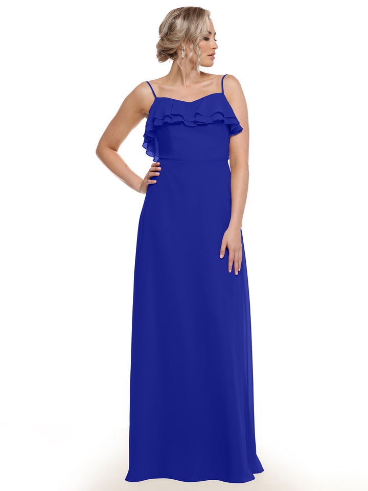 A woman models Avery Austin’s 80146—a long, royal blue chiffon A-Line dress with thin straps and tiered ruffles—posing with one hand on her hip against a white background.