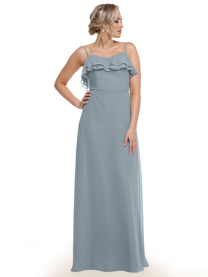 A woman wearing Avery Austin’s 80146 light blue chiffon A-line dress with spaghetti straps and tiered ruffles stands against a white background, looking to the side with one hand on her hip.