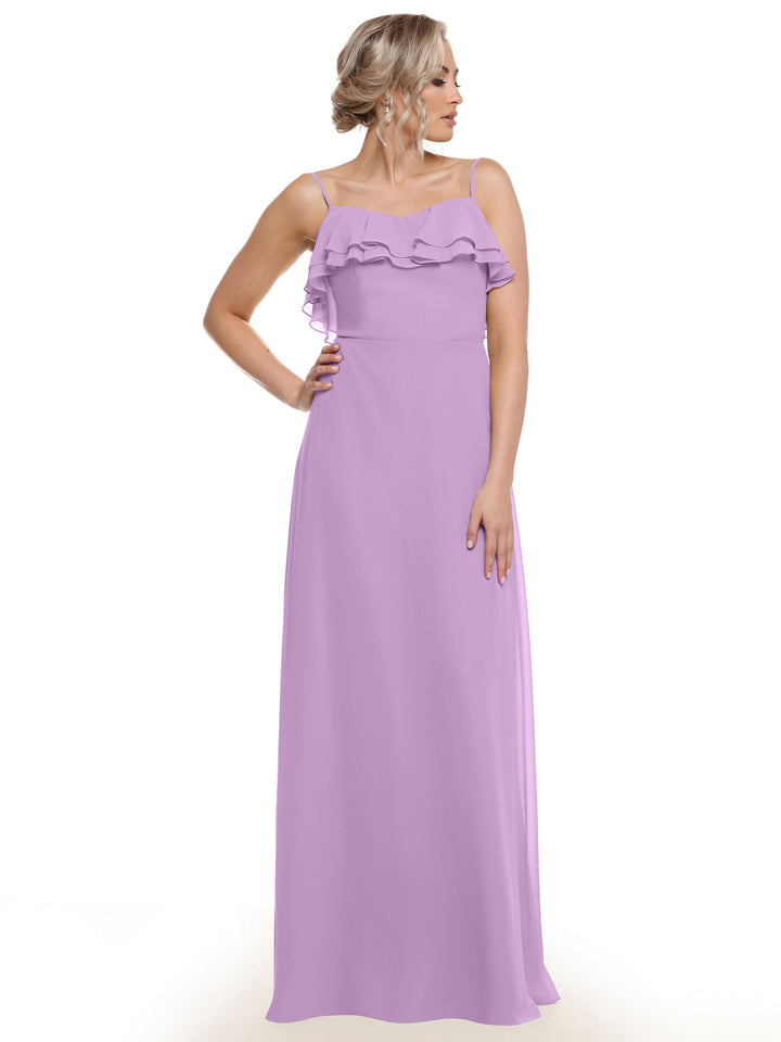 A woman wearing Avery Austin’s 80146—a long chiffon A-line dress with tiered ruffles and a dimensional bodice—stands against a plain white background, her hair styled in an elegant updo.