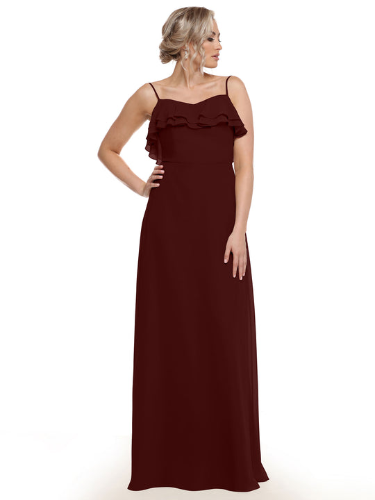 A woman in Avery Austin’s 80146 wears a sleeveless, floor-length burgundy chiffon A-line dress with thin straps and tiered chest ruffles, standing before a white background, her hair styled in an elegant updo.