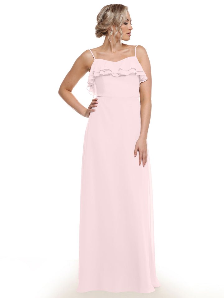 A woman in the Avery Austin 80146 sleeveless light pink chiffon A-line dress with tiered ruffles at the neckline stands against a white background, looking right with one hand on her hip.