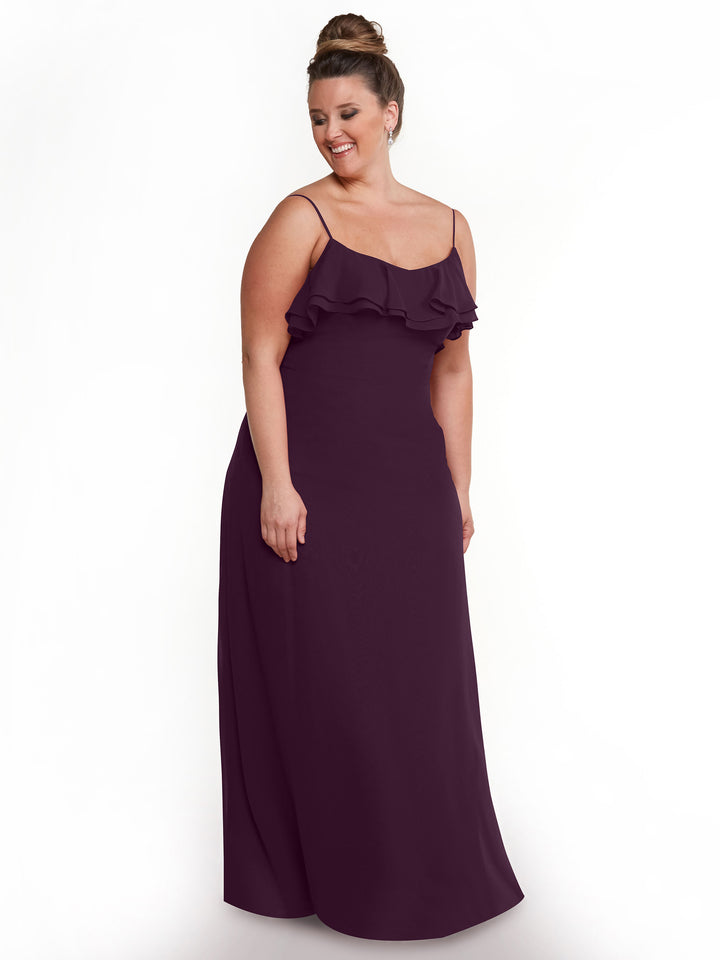 A woman models Avery Austin 80146, a floor-length sleeveless A-line dress in dark purple chiffon with thin straps and a ruffled neckline. Tiered ruffles enhance its elegant look as she stands against a white background, smiling.
