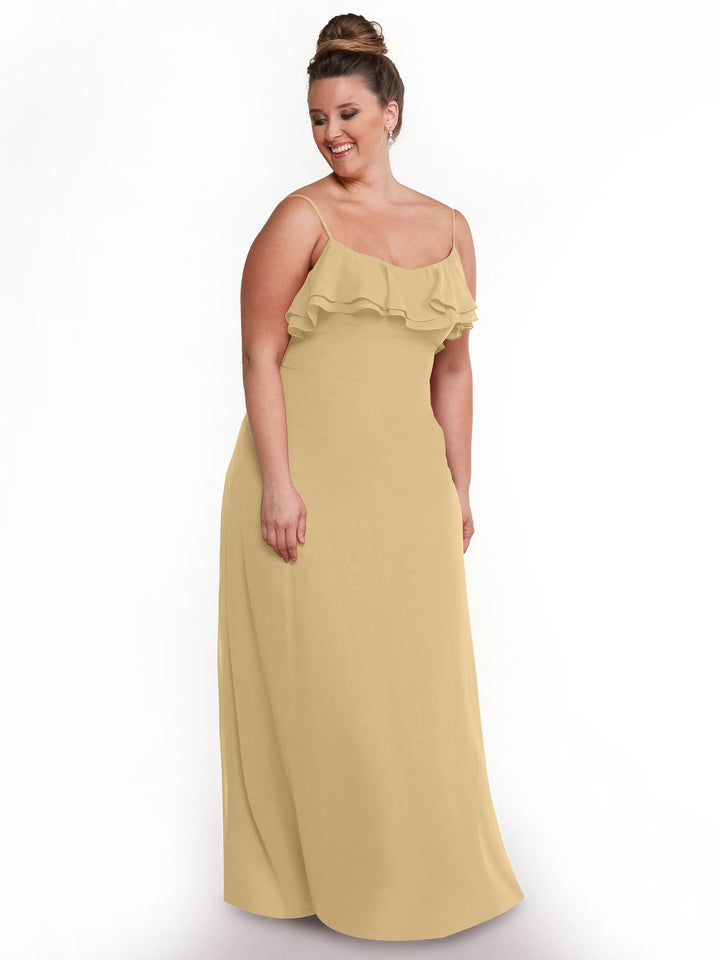 A woman with brown hair in a bun models Avery Austin’s sleeveless, light yellow chiffon A-Line dress (style 80146) with tiered ruffles on the bodice. She smiles while standing against a plain white background, looking slightly to the side.