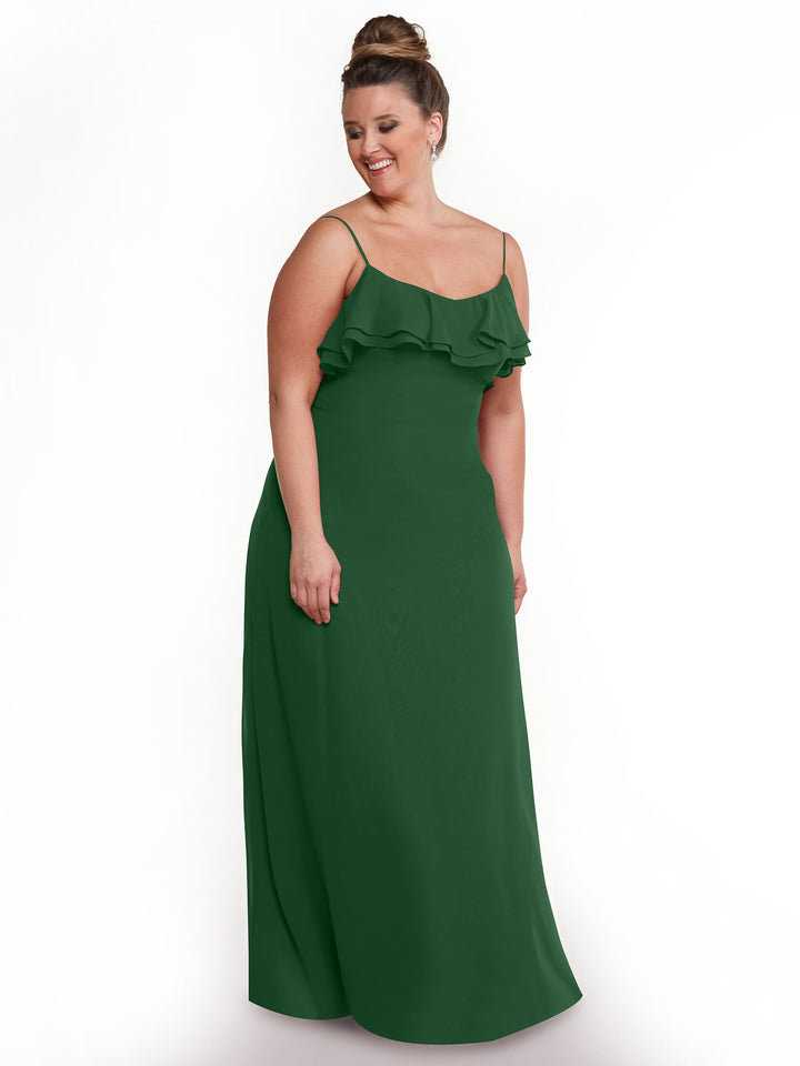 A woman wears the Avery Austin TH-80146: a floor-length, sleeveless green chiffon A-line dress featuring thin straps and a ruffled neckline, standing with a smile and looking down to the side against a plain white background.