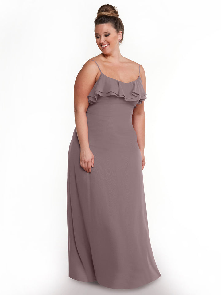 A woman in the Avery Austin 80146 mauve chiffon A-line dress with spaghetti straps and ruffled bodice stands against a white background, smiling and looking to the side.