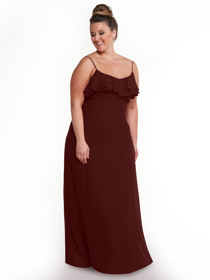 A woman models Avery Austin’s sleeveless, floor-length maroon chiffon A-Line dress (style 80146) with ruffle bodice detail, standing against a plain white background, smiling and looking down to her left.