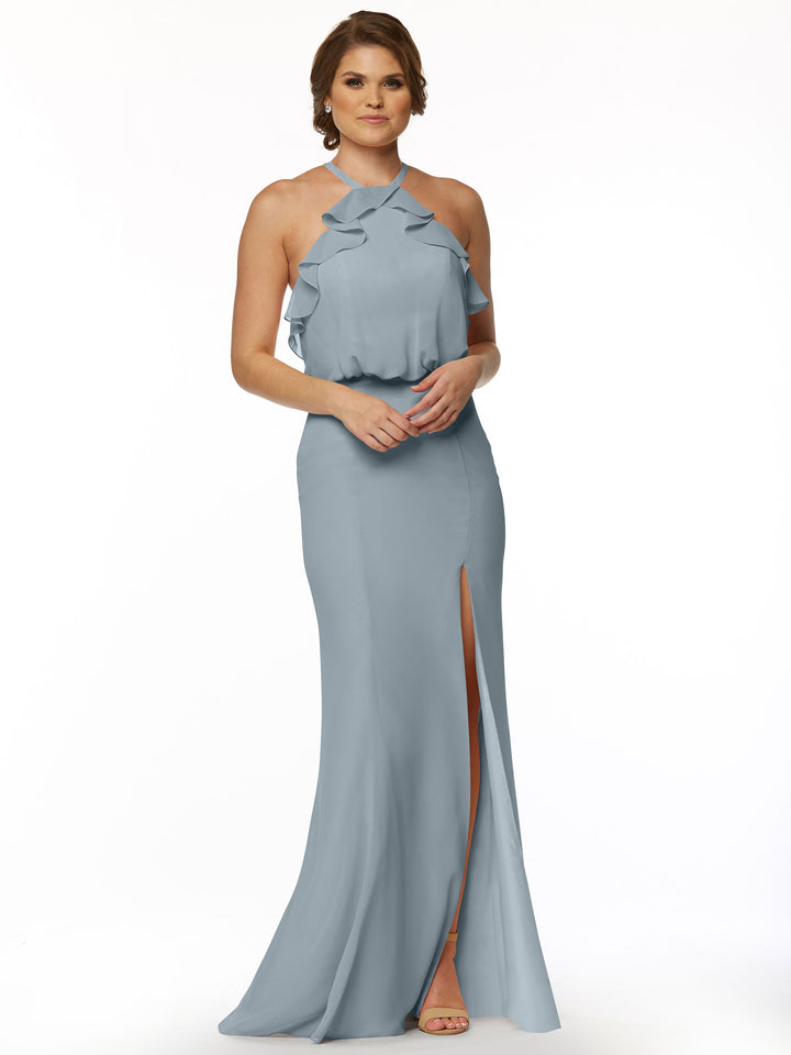 A woman with short, wavy brown hair models Avery Austin’s 80147: a sleeveless, fitted chiffon dress featuring ruffle details and a thigh-high side slit. She stands against a white background wearing open-toe shoes.