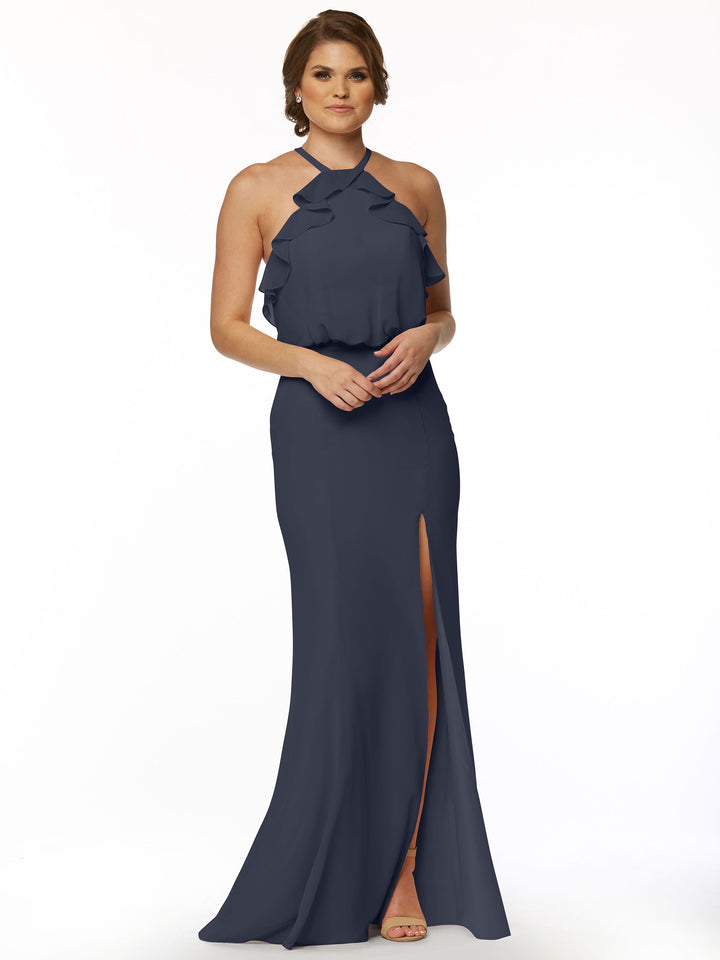 A woman with short brown hair and open-toed shoes poses against a white background, wearing Avery Austin style 80147—a sleeveless, floor-length navy blue fitted chiffon dress featuring a ruffled halter top and front slit.