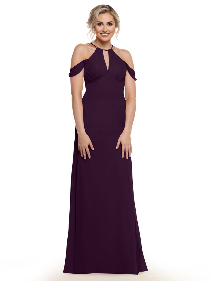 A woman wearing the Avery Austin 80148, a floor-length dark purple gown with chiffon cap sleeves and a keyhole neckline, stands and smiles against a plain white background.