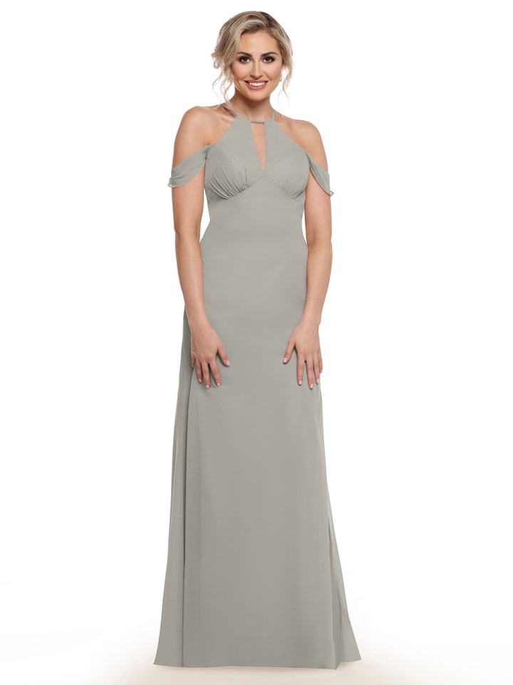 A woman with blonde hair in an updo models Avery Austin’s long, light gray chiffon cold-shoulder gown (style 80148) with cap sleeves and a keyhole neckline, standing against a plain white background.