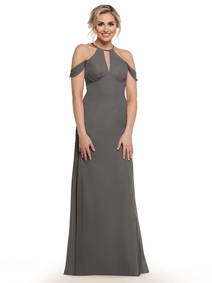 A woman stands smiling against a white background wearing Avery Austin’s 80148, a floor-length gray gown with chiffon cap sleeves and a keyhole neckline.